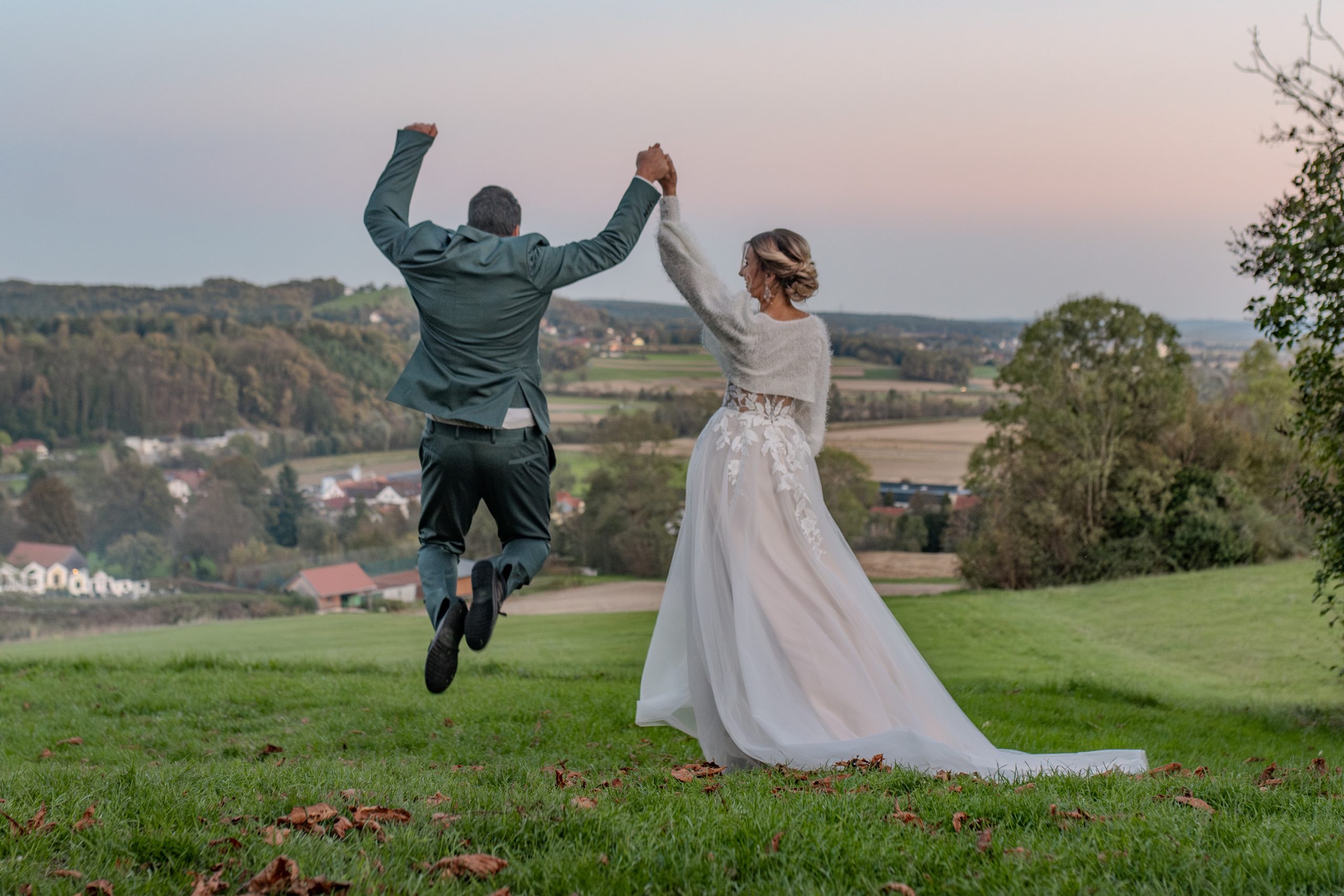 Brautpaar springt vor der Hügellandschaft der Oststeiermark – Hochzeit am Landgut Riegerbauer