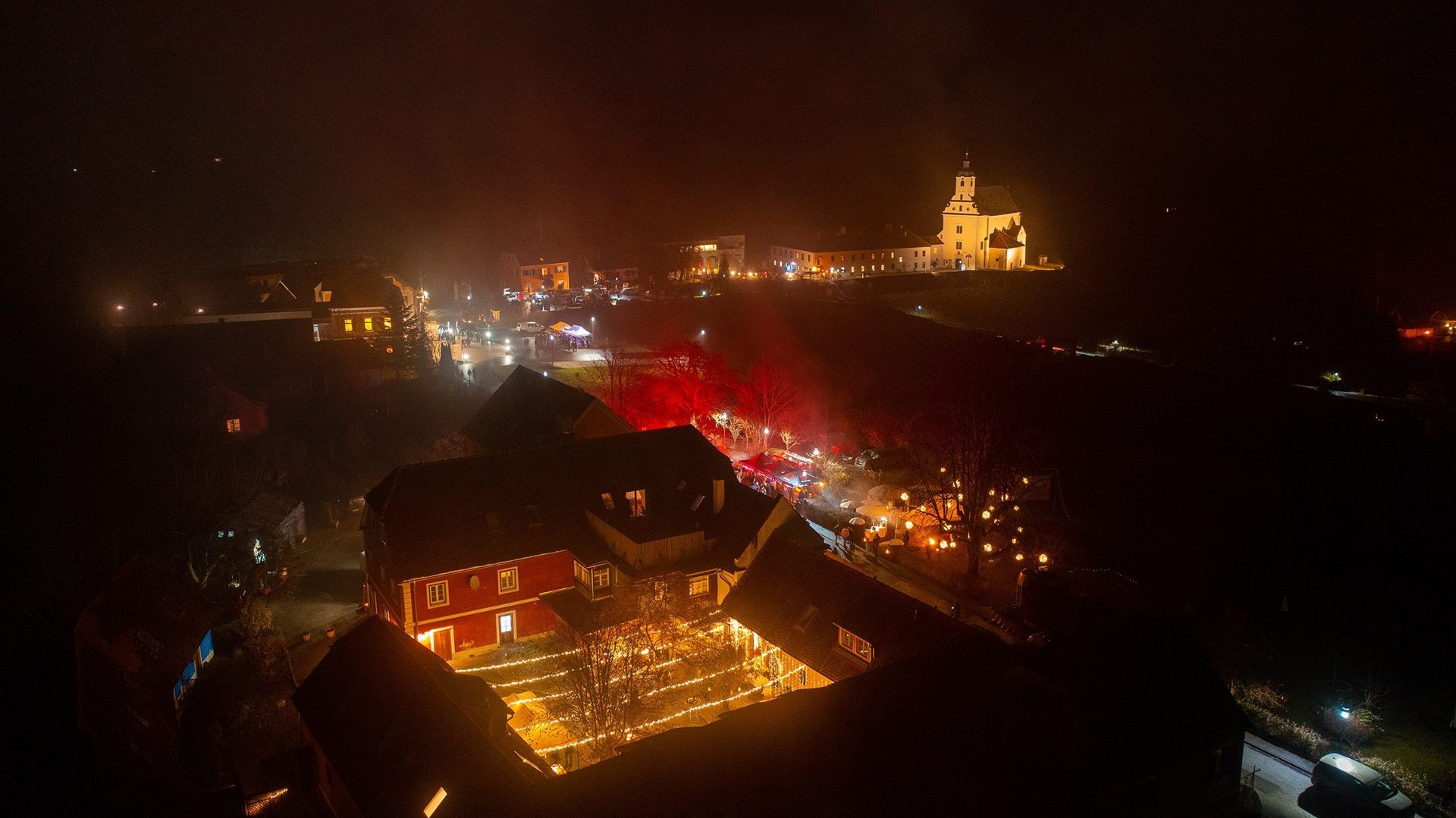 St. Johanner Gassladvent bei Nacht: beleuchteter Hof und Kirche St. Johanner Gassladvent bei Nacht: beleuchtete Marktstände, Landgut Riegerbauer und Pfarrkirche im Nebel