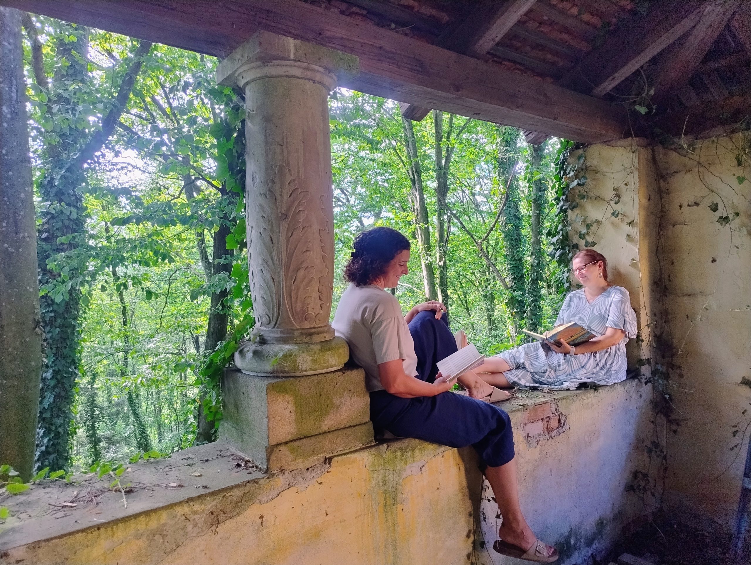 IMG_20260729_164410875_HDR_AE Zwei Personen lesen in einer alten Waldruine in der Umgebung des Landgut Riegerbauer